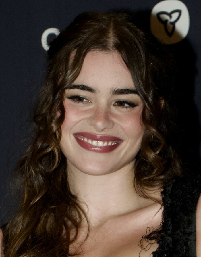 Barbie Ferreira smiling with curly hair and wearing a black outfit at an event, highlighting her career.