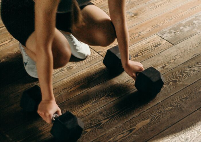 Person holding dumbbells on wooden floor, illustrating horrible gifts people say they'd rather not receive.
