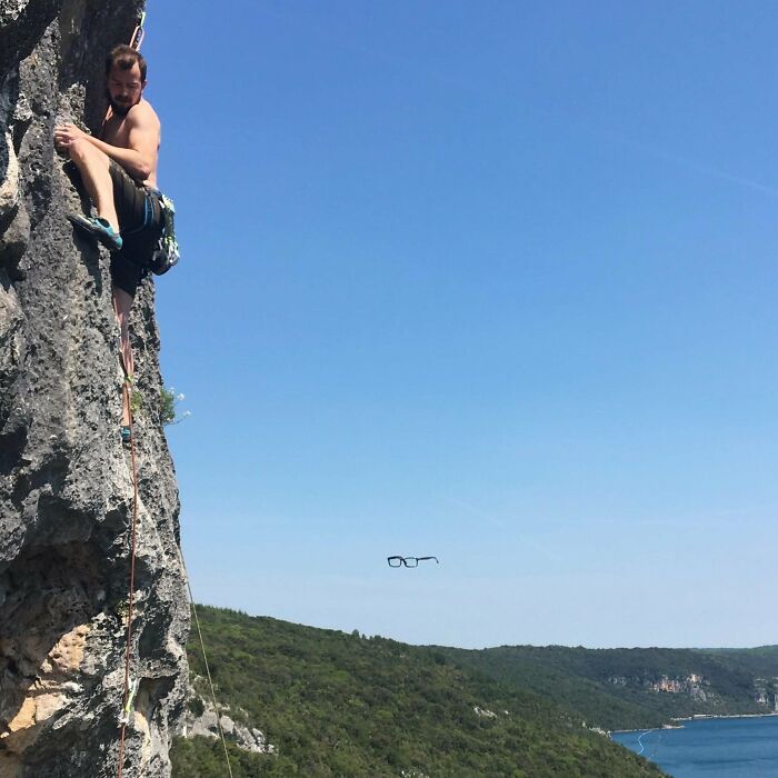 Man rock climbing outdoors with glasses seemingly floating in midair, a funny and interesting perfect timing pic.