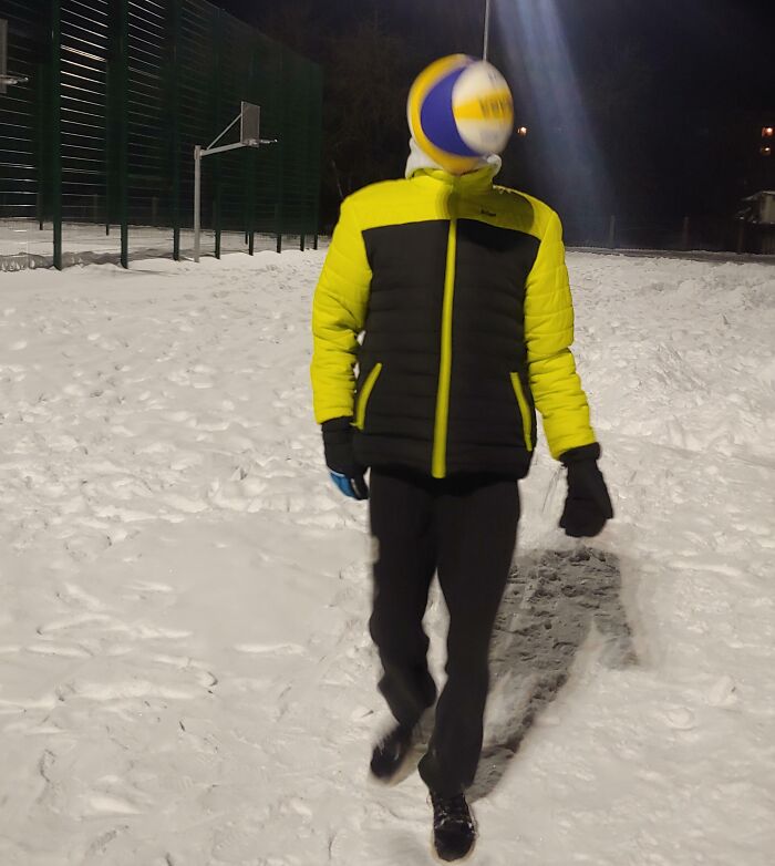 Person wearing a yellow and black jacket with a volleyball perfectly timed to cover their face in a funny, interesting, and weird pic.