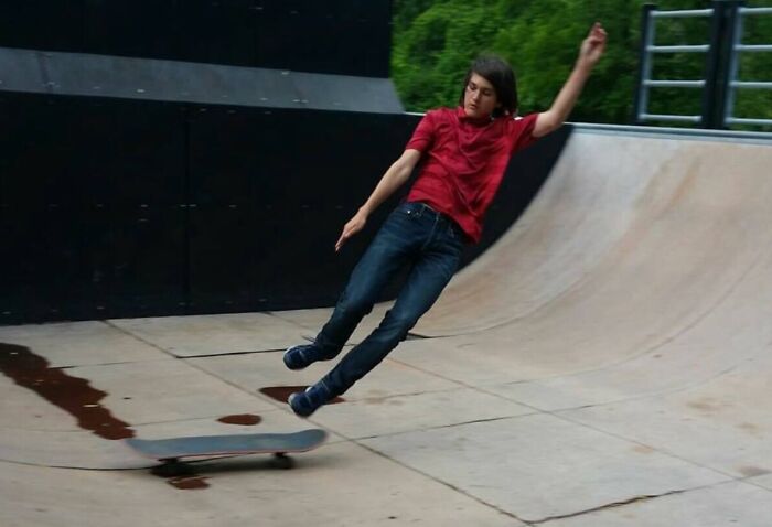 Teenager in a red shirt captured at the perfect time falling off a skateboard in a skatepark, funny and interesting moment.