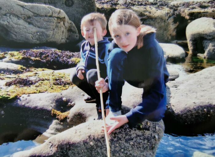 Two kids playing with a stick on rocks near water, captured in a funny and interesting perfect timing pic.