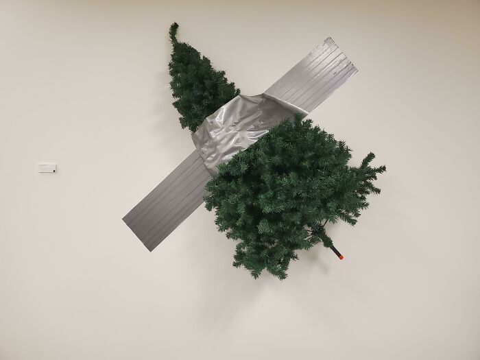Creative workplace Christmas decoration shows upside-down tree duct taped to a plain wall, impressing with unique holiday design.