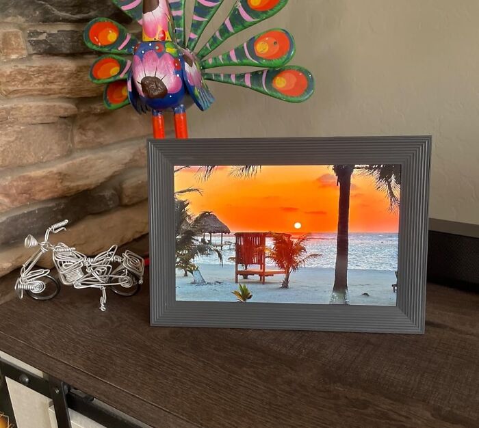 Colorful peacock figurine and wire motorcycle beside framed beach sunset photo, useful presents for favorite child ideas.