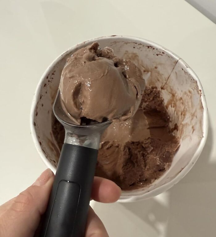 Hand holding an ice cream scoop with chocolate ice cream from a partially empty container, a useful present idea.