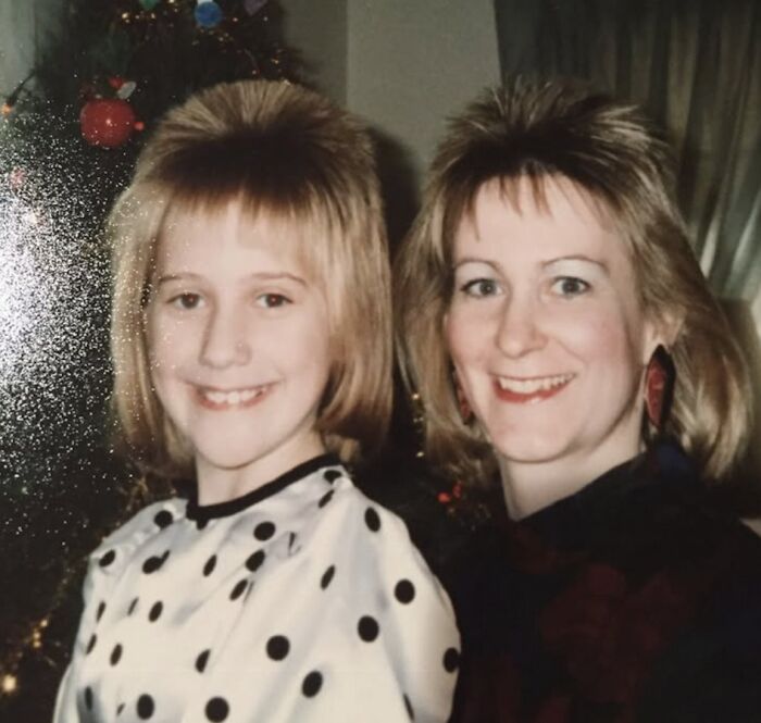 Awkward family Christmas photo with mother and daughter smiling, showcasing retro hairstyles and festive background decorations.