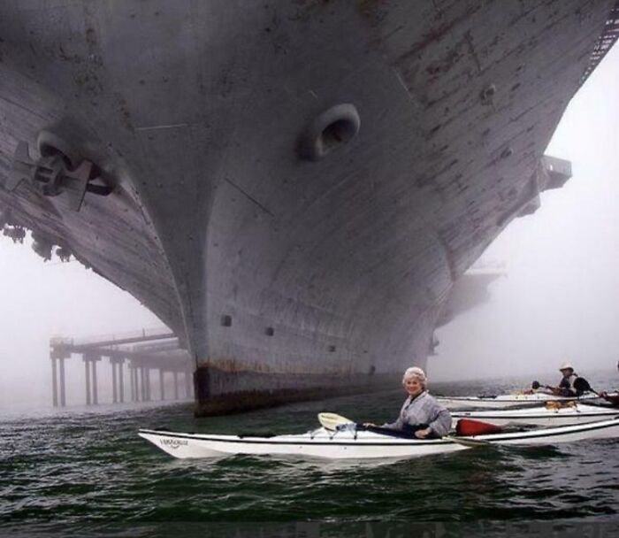 Kayakers paddling near the massive hull of a ship, showcasing an intense example of megalophobia-inducing scale and size.