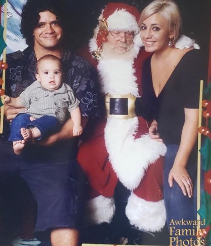 Family awkward Christmas photo with a baby, young parents, and a Santa Claus looking unamused during holiday photo session.