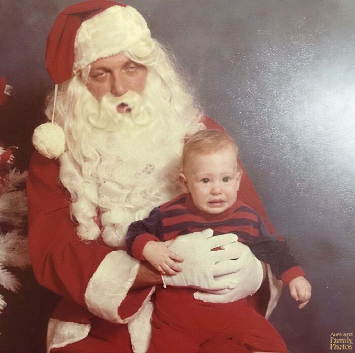 Awkward family Christmas photo with a distressed child sitting on a tired Santa Claus’s lap during holiday photo session.