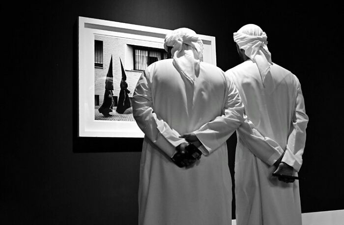 Two men in traditional clothing observe a black-and-white photo capturing magical street moments in daily life.