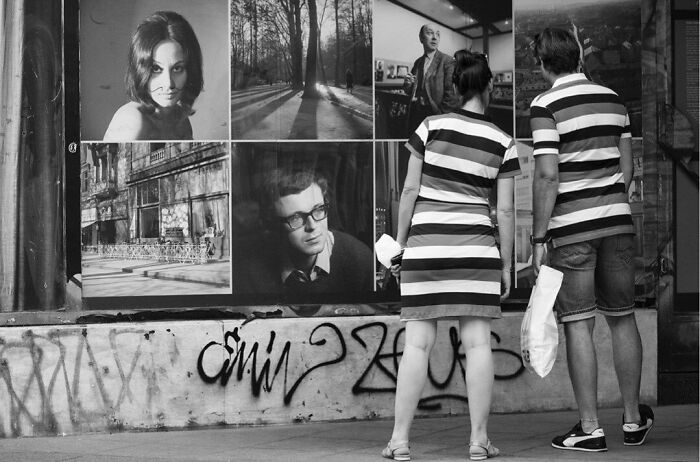 A couple admiring street art photos, capturing the marvels of daily life in an urban setting with a magical feel.