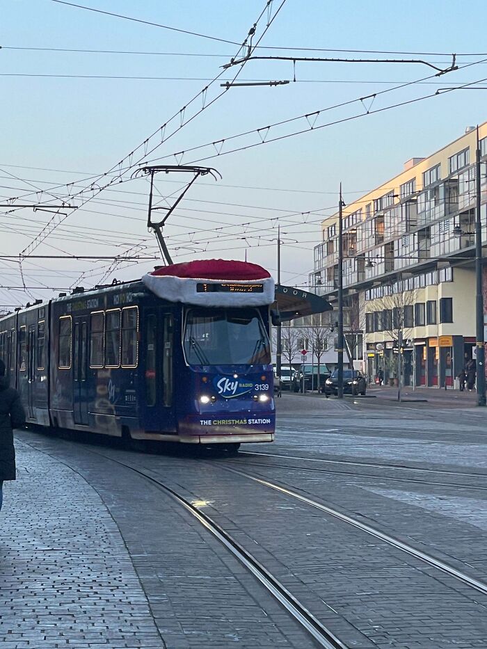Tram decorated with a large Santa hat on top, showcasing creative Christmas decorations in a public urban setting.
