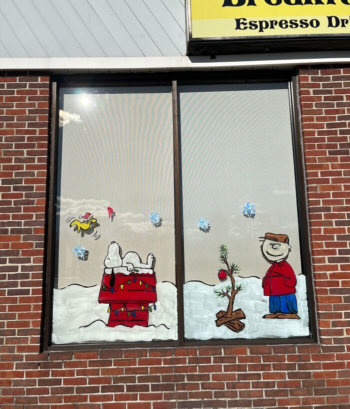 Creative workplace Christmas decoration on window featuring Snoopy and Charlie Brown with holiday elements and snowflakes.