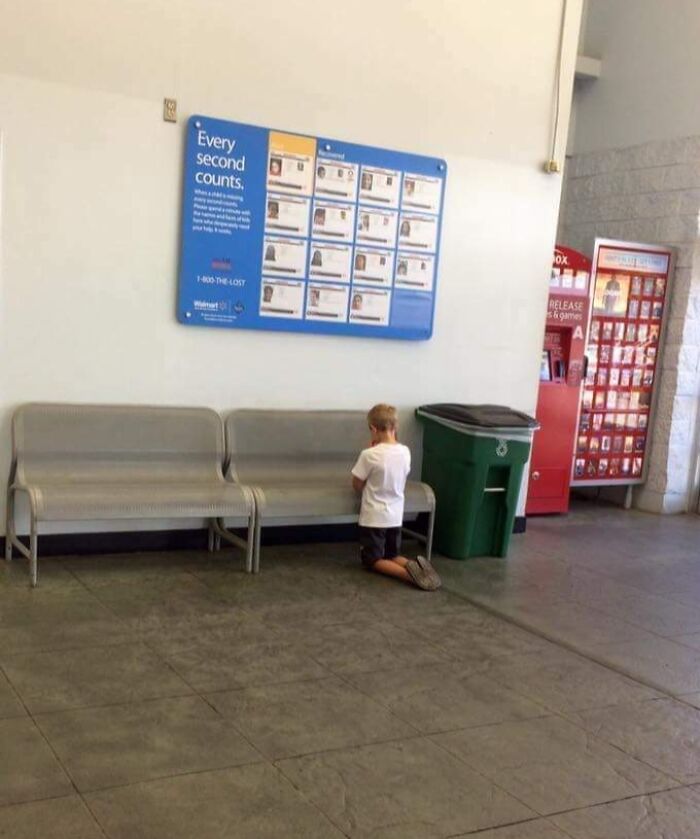 Young boy kneeling alone near a bench inside a Walmart store with a missing persons board on the wall.