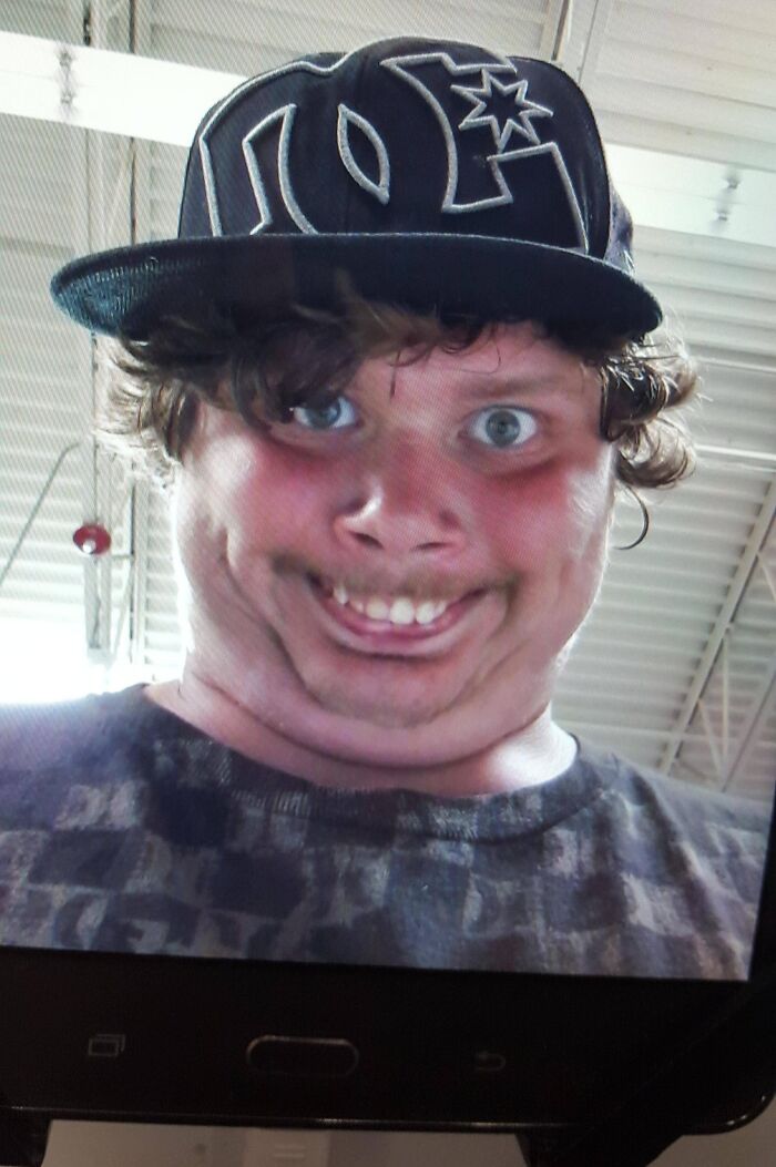 Close-up selfie of a young man with a distorted face wearing a DC hat inside a Walmart store environment.