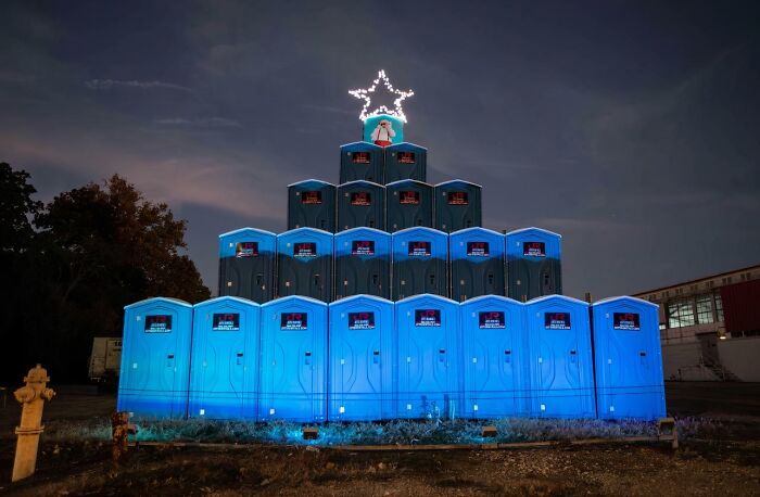 Creative workplace Christmas decorations featuring portable toilets arranged as a festive tree with a glowing star on top at night.
