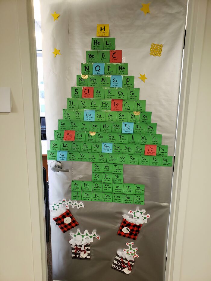 Creative workplace Christmas decoration with a periodic table shaped like a tree and festive stockings on a office door.