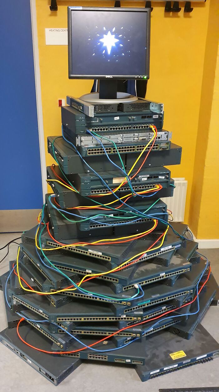 Creative workplace Christmas decoration made of stacked computer servers and colorful network cables arranged like a Christmas tree.