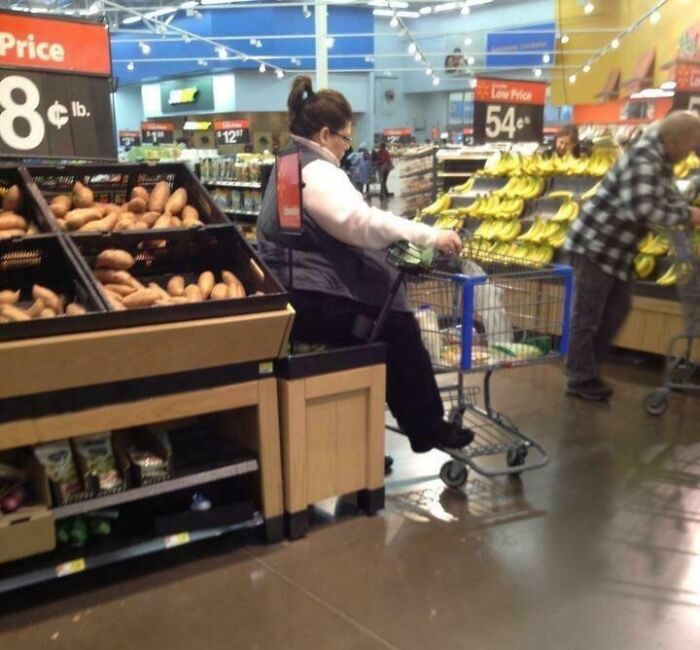 Woman using motorized shopping cart near produce section in a Walmart store with bananas and sweet potatoes displayed.