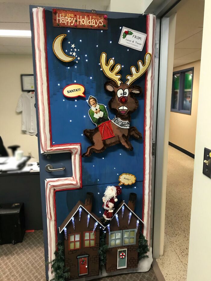 Office door decorated with creative Christmas decorations featuring a reindeer, Santa, festive houses, and holiday lights.