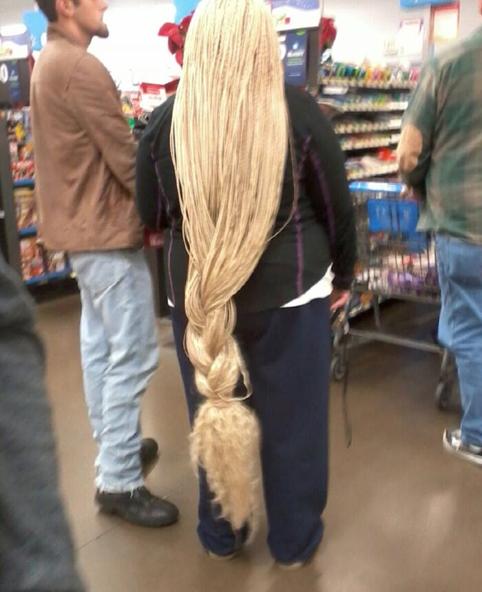 Woman with extremely long braided hair shopping inside Walmart, surrounded by other customers and carts.