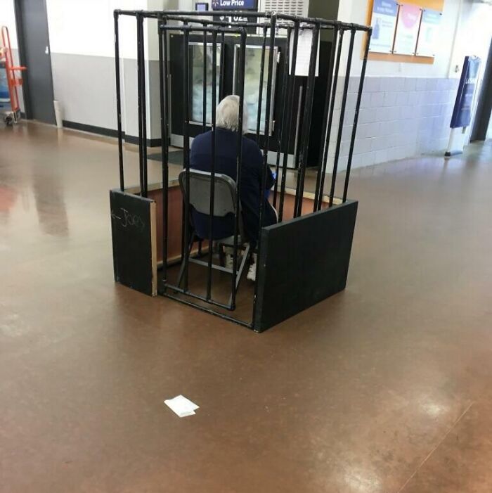 Security guard sitting inside a small cage-like booth at a Walmart store, creating an unusual scene.