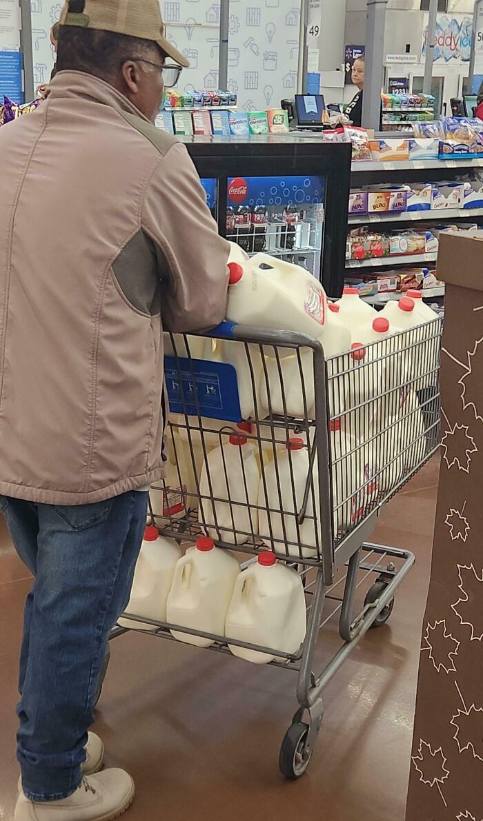 Man pushing Walmart shopping cart filled with multiple gallons of milk inside the store aisles.