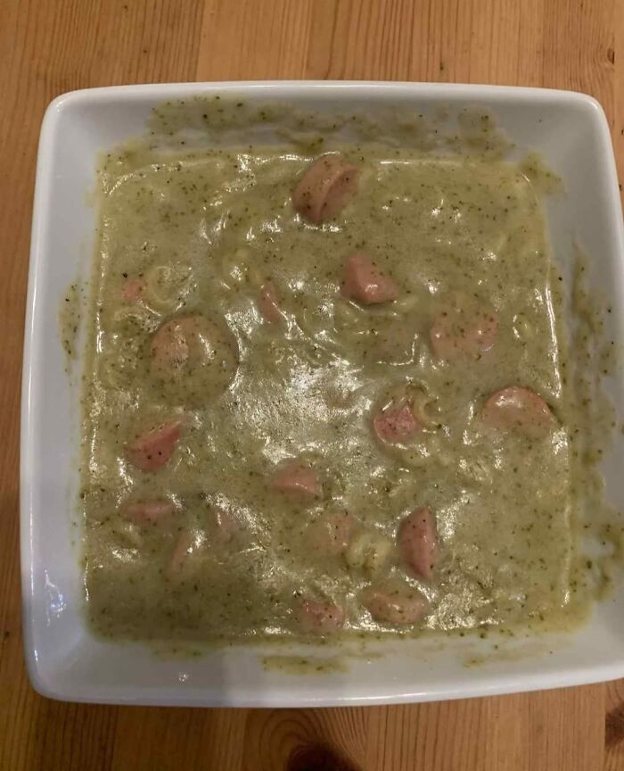 Bland looking green soup with chunks of sausage in a white bowl on a wooden table, food pics to be shamed.