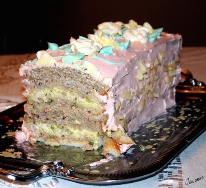 Partially eaten layered cake with pink frosting and decorative icing on a serving tray, a food pic that deserves to be shamed.