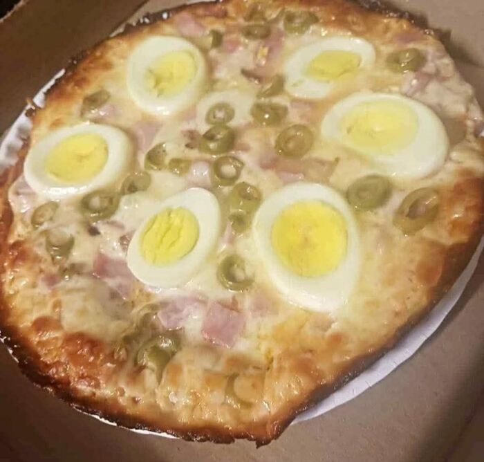 Pizza topped with hard-boiled egg slices and green olives in a poorly presented food pic for online shaming