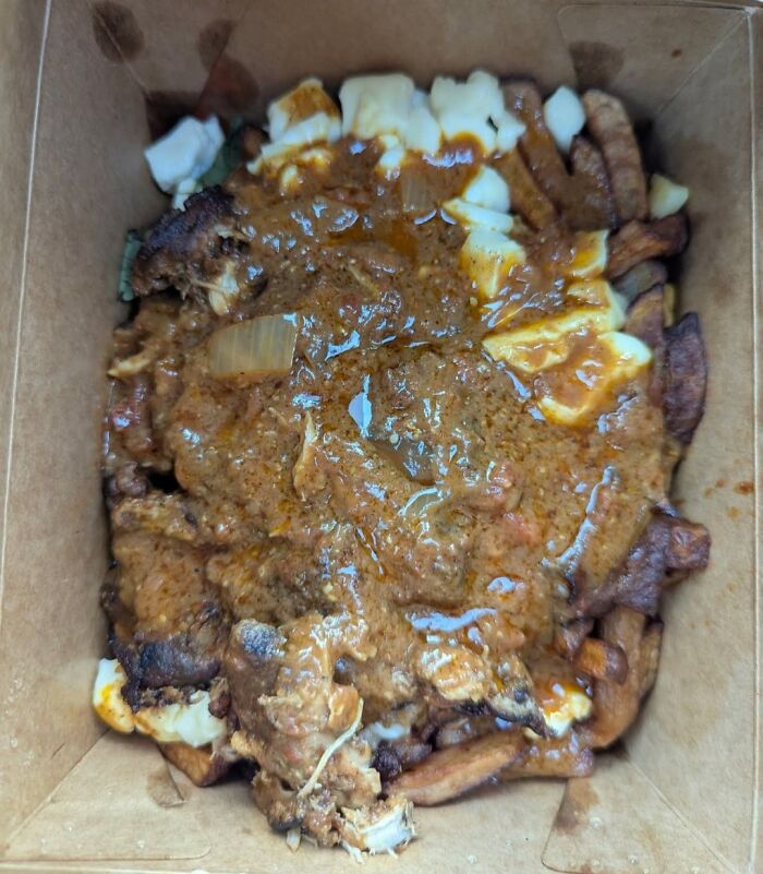 Overly oily curry chicken poutine with fries and cheese curds in a cardboard takeout container, food pics to be shamed online.