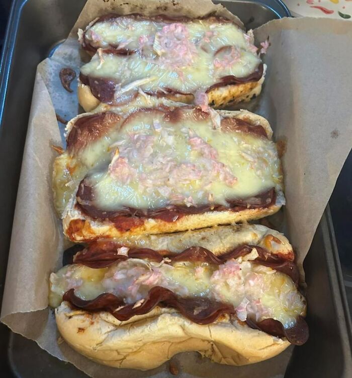Three homemade submarine pizza sandwiches with melted cheese, pepperoni, and chopped onions in a baking tray.
