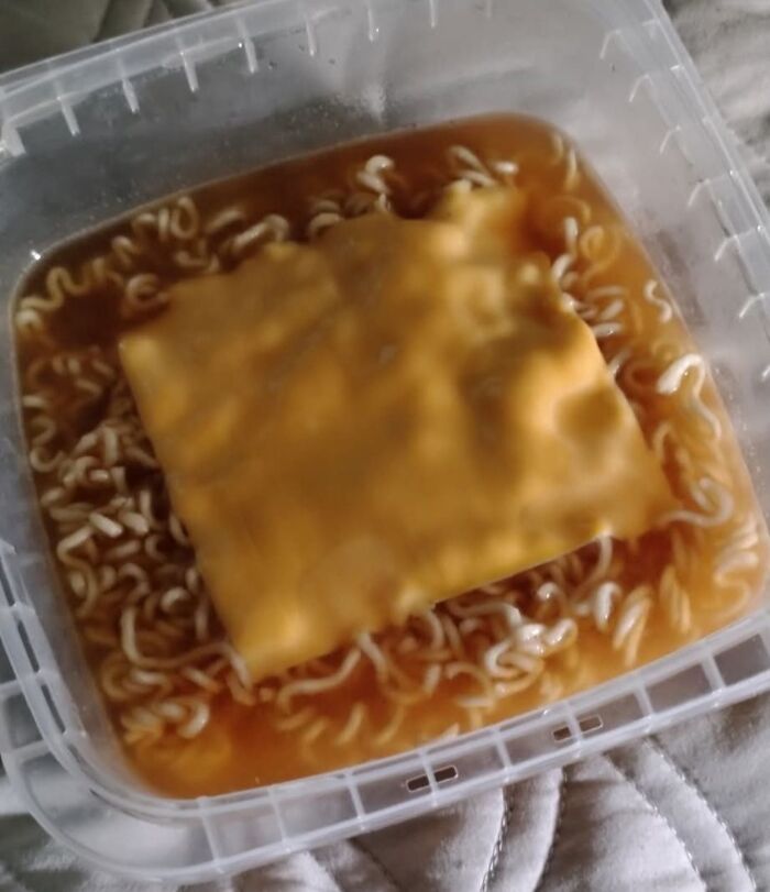 Ramen noodles in plastic container topped with a slice of processed cheese, an unusual food combination.