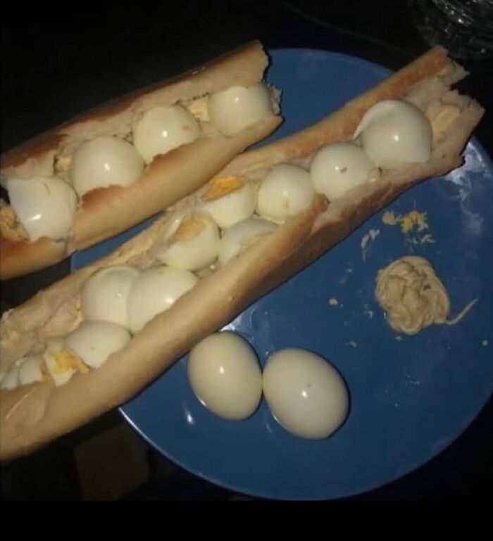 Two baguette sandwiches filled with peeled boiled eggs and a small dollop of mustard on a blue plate, food pics to be shamed.