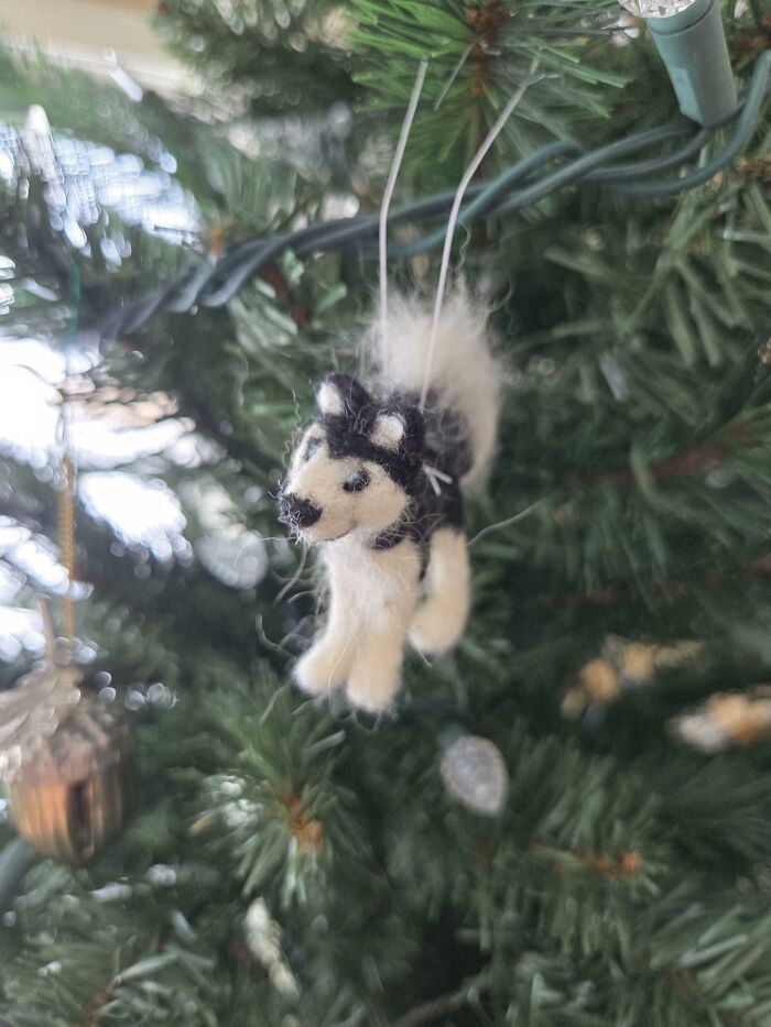 Creative Christmas decoration of a felted husky hanging on a green artificial tree with string lights in the background.