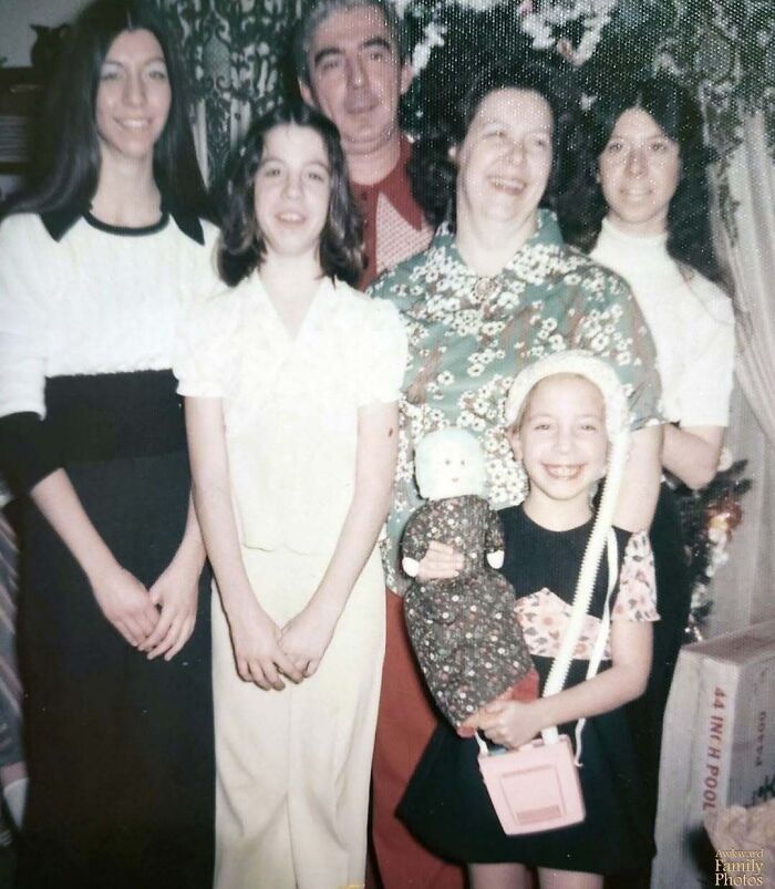 Family posing awkwardly for a vintage Christmas photo with a decorated tree and wrapped presents in the background.