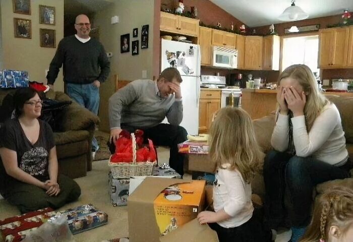 Family awkward Christmas photo with adults and children reacting humorously in a living room filled with holiday gifts.