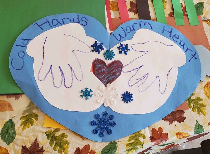 Child's funny drawing of cold hands with warm heart, featuring hand outlines and decorative snowflakes on a blue heart background.