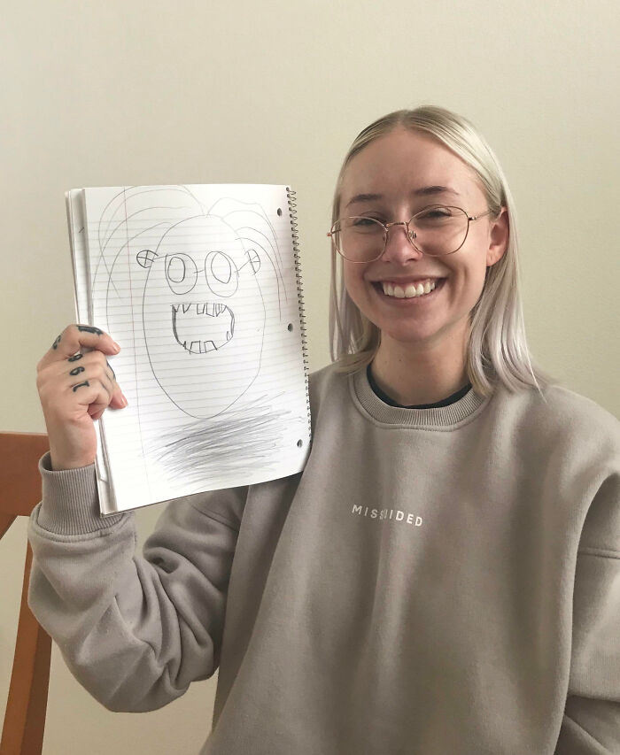 Smiling woman wearing glasses holding a funny and flattering portrait drawing by kids with no filter whatsoever.