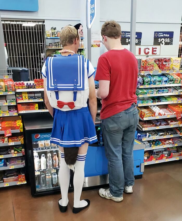 Person dressed in a blue sailor outfit with a tail shopping at a Walmart checkout with another customer nearby.