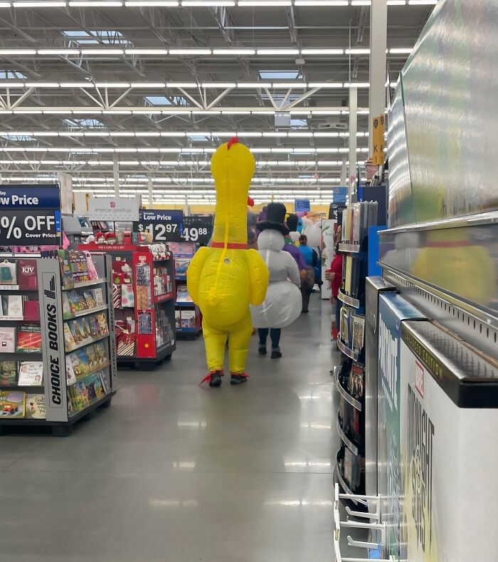 People in inflatable costumes walking down an aisle inside a Walmart store, creating a curious shopping scene.