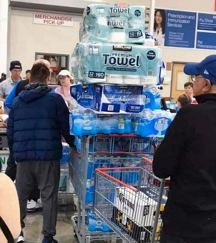 Shoppers with overloaded carts stacked with bottled water and paper towels inside a Walmart store checkout area.