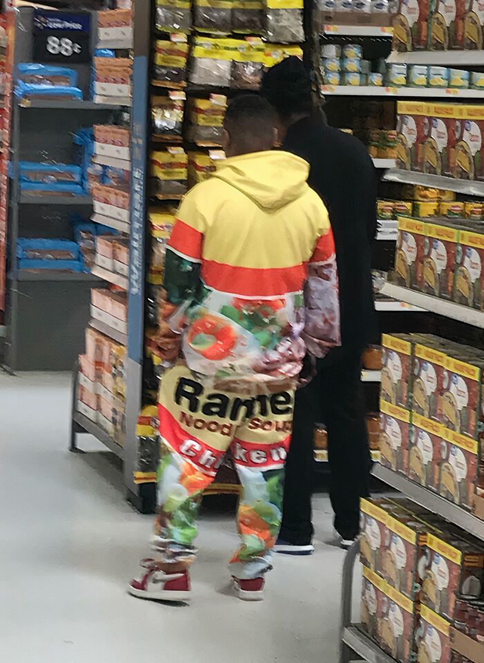 Two shoppers browsing aisles in a Walmart store with one wearing colorful ramen noodle soup outfit.