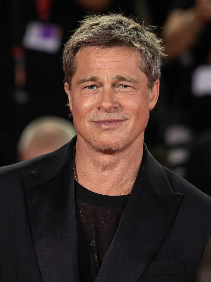 Brad Pitt smiling on the red carpet wearing a black jacket at a formal event, showcasing his career highlights.