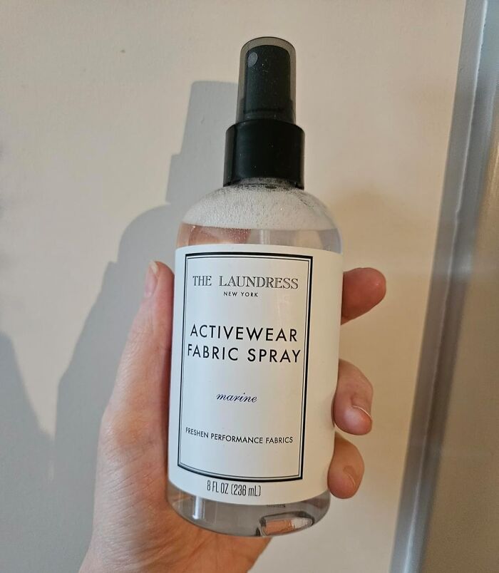 Hand holding The Laundress activewear fabric spray bottle, a unique host gift idea for saying thank you.