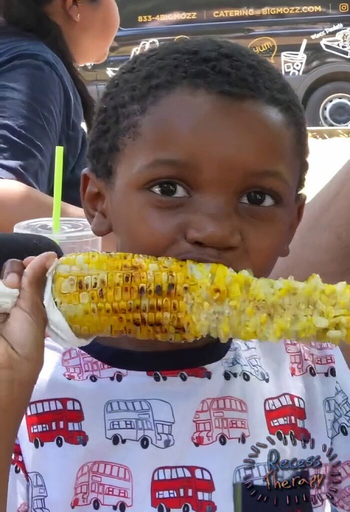 Child eating grilled corn, captured candidly, showcasing moments that made people viral and internet icons randomly.