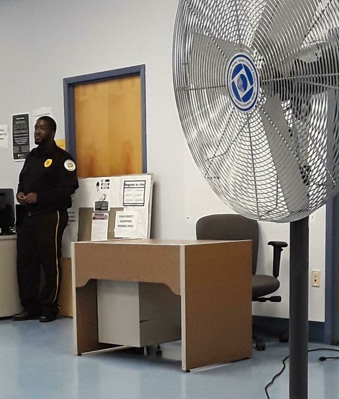 Security guard standing by a desk while giant floor fan dominates foreground, next-level jerks