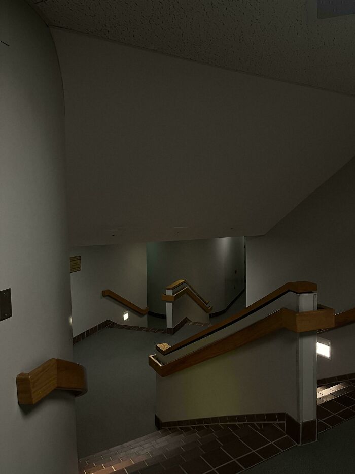 Dimly lit empty stairwell with wooden handrails in a dim hallway, evoking creepy liminal spaces like the backrooms.