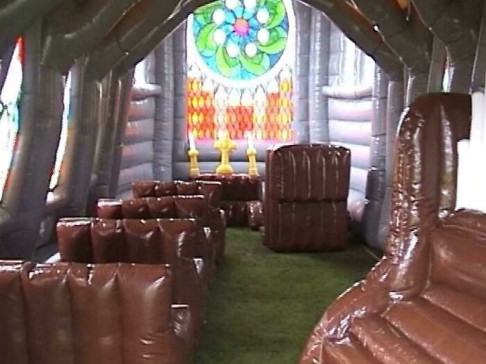 Inflatable church interior with stained glass windows and brown cushioned seating in a creepy liminal space setting.