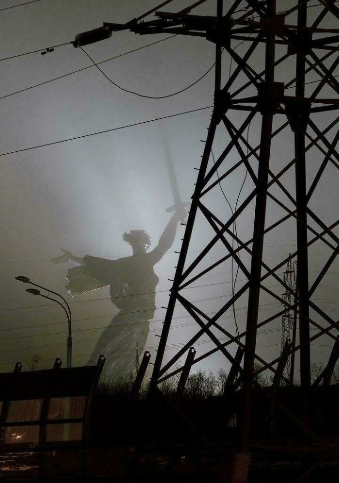 Ghostly statue silhouette behind power lines and poles in a foggy landscape, evoking creepy liminal spaces vibe.